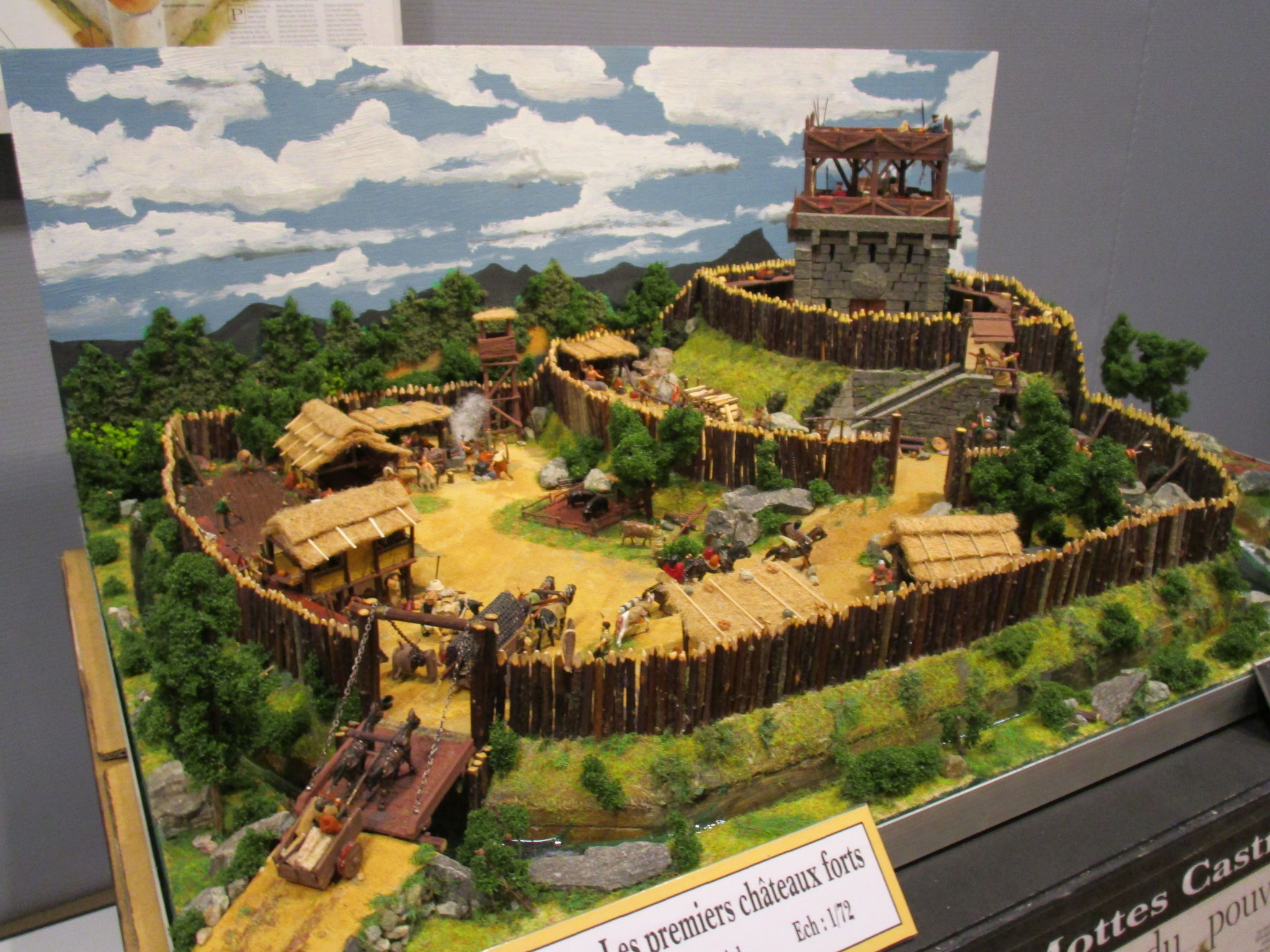 Maquette d’une motte castrale, avec une tour, des palissades, un pont et des maisons.